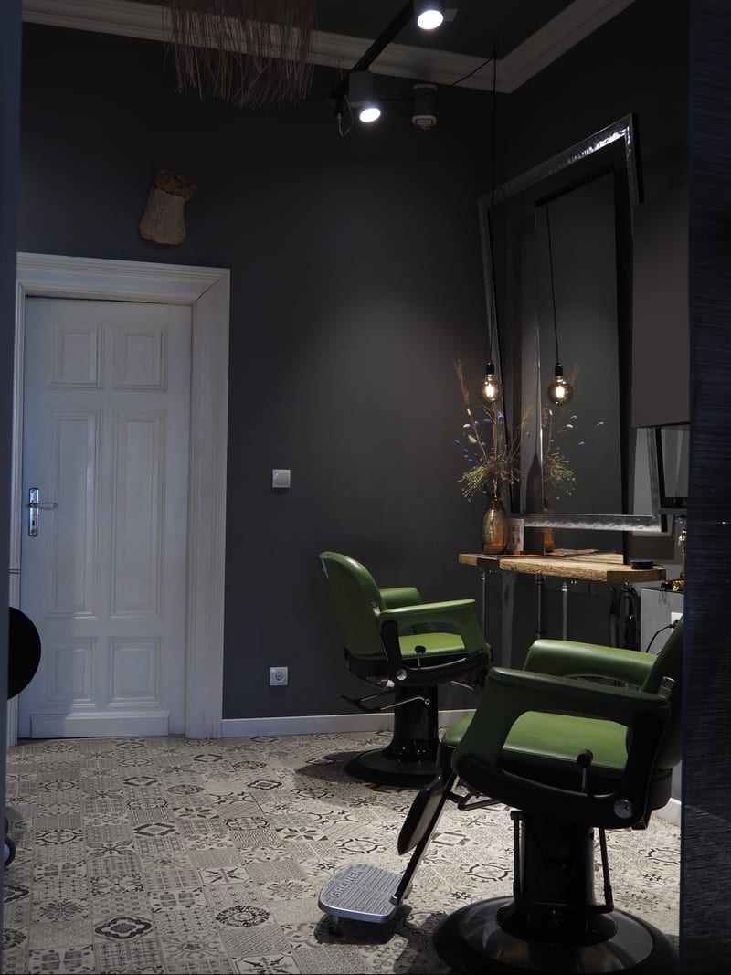 Salonraum mit weißer Altbautür, grünen Barbierstühlen und Mosaikboden